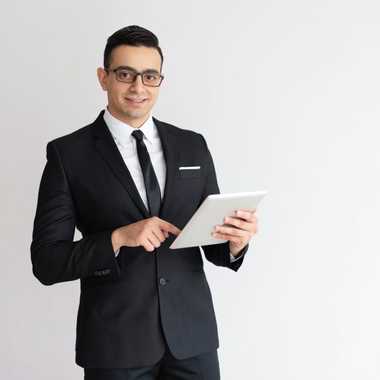 Cheerful young businessman checking email on tablet and looking at camera. Positive successful entrepreneur using gadget as personal organizer. Technology concept